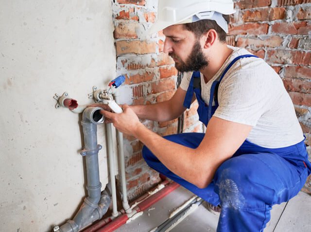  a plumber applying sealant on a sewer pipe on the wall 