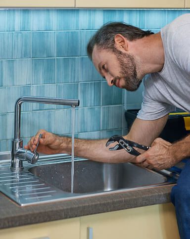 a plumber inspecting a leaky kitchen faucet